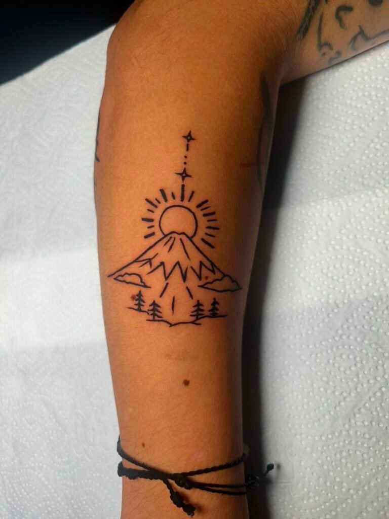 Fine line mountain and sun tattoo on forearm done at Tinta y Pinta Tattoo Quito